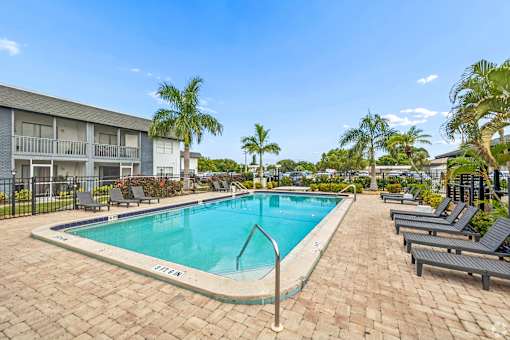 A pool surrounded by lounge chairs and palm trees.
