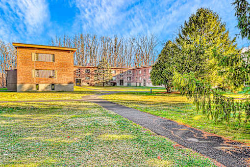 A small building sits in a grassy field with a paved walkway leading to it.