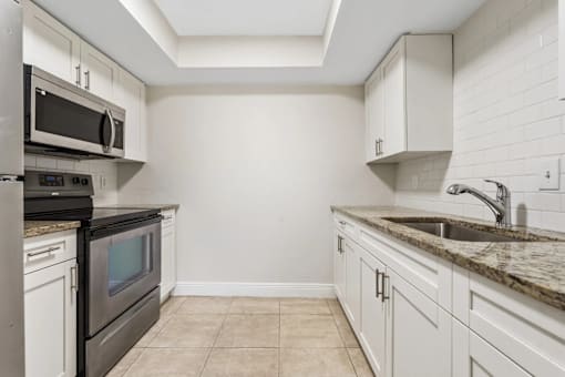 A kitchen with white cabinets and a black microwave.