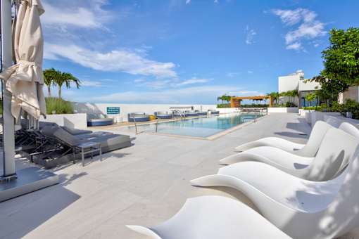 A pool area with white chairs and a clear blue sky.