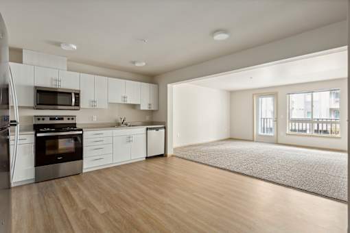 an empty kitchen and living room with white cabinets and stainless steel appliances