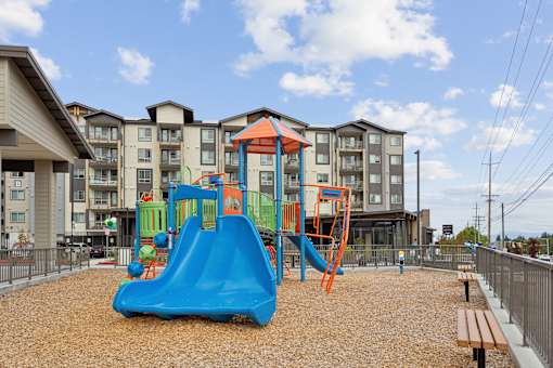 a playground with a swing set and slides in front of an apartment building