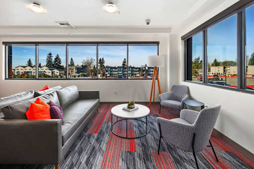 A living room with a grey couch, a grey chair, a round coffee table, and a large window with a view of the outside.