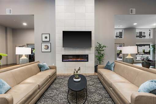 A living room with a tan couch, a black coffee table, and a flat screen TV mounted above a fireplace.