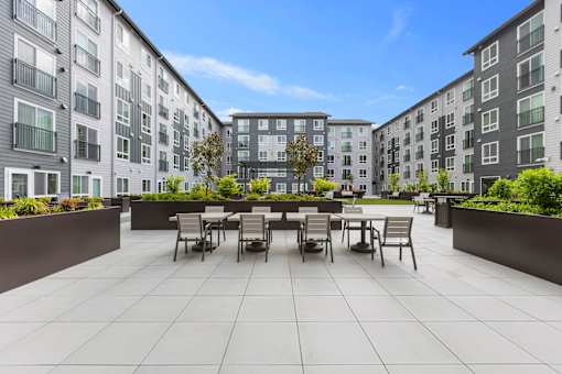 A patio with chairs and a table is surrounded by apartment buildings.