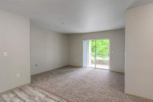 A room with a carpeted floor and a sliding glass door leading to a balcony.