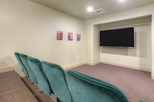 A room with a row of green chairs and a black screen on the wall.