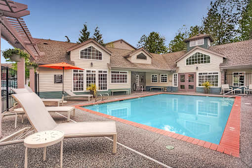 A pool and lounge chairs are in front of a house.