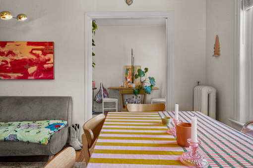 A dining table with a yellow and pink striped table runner and pink candles on it.