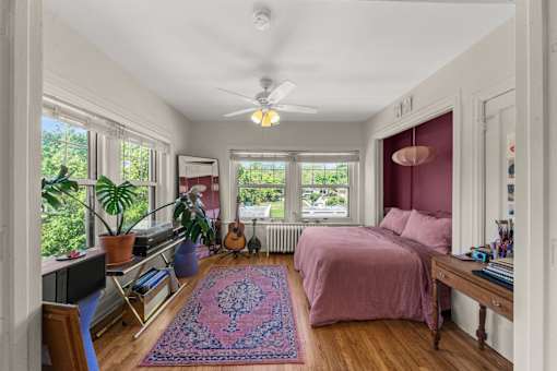A bedroom with a bed, a chair, a guitar, a potted plant, and a rug.
