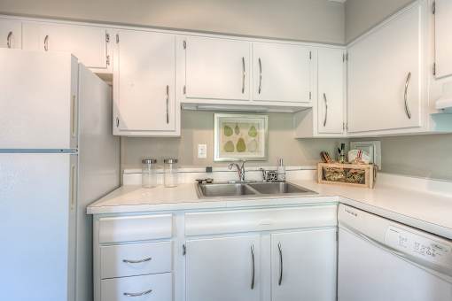 A white kitchen with a sink and a refrigerator.