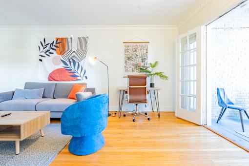 A blue chair sits in a room with a grey couch and a wooden table.