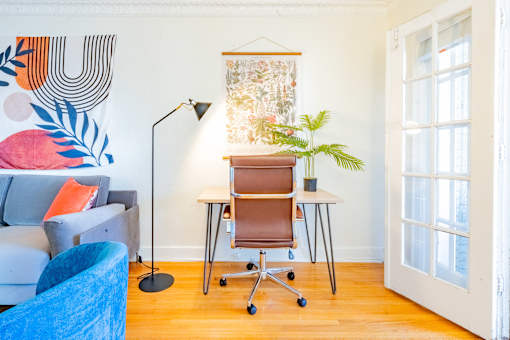 A blue chair sits in a room with a white couch and a desk with a chair.