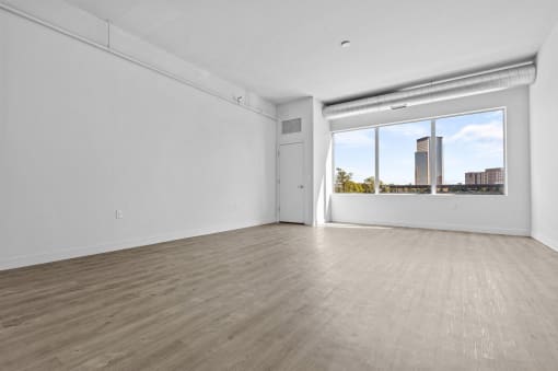 an empty living room with a large window and hardwood floors
