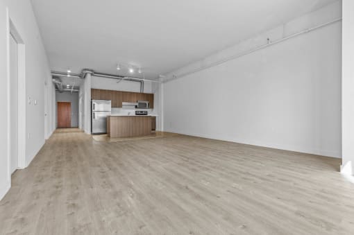 an empty living room and kitchen with wood floors and white walls