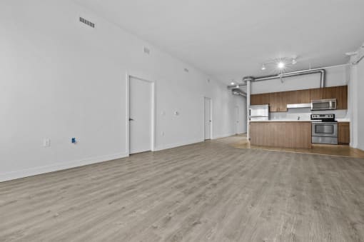 an empty living room and kitchen with wood floors and white walls