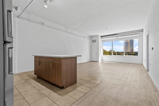 an empty living room with a kitchen and a large window