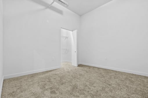 a bedroom with white walls and carpet and a door to a closet