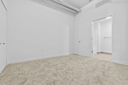 a bedroom with white walls and carpet and a door to a closet