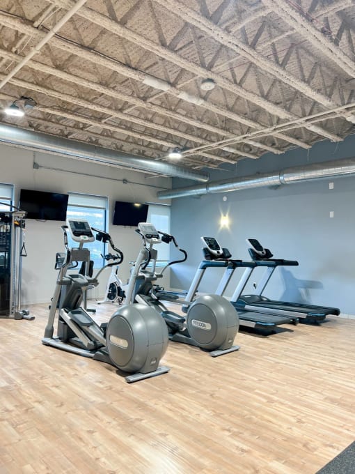 a gym with cardio equipment and weights on a wooden floor