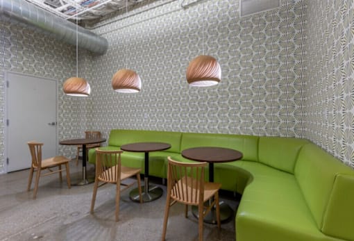 A room with a green couch, wooden chairs and tables with hanging lights.