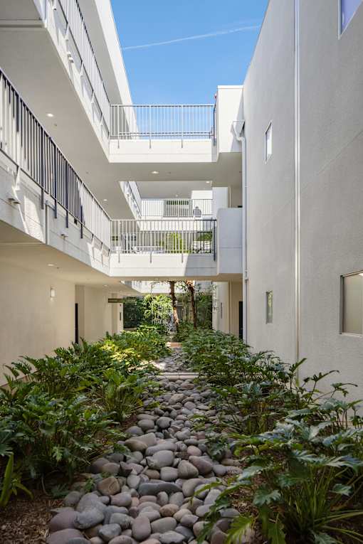 A long pathway with rocks and plants on either side leads to a balcony.
