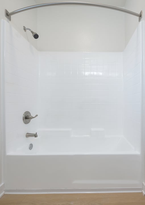 A white tiled shower with a silver shower head and faucet.