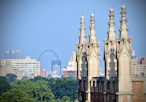 A cityscape with a large arch in the background and a building in the foreground.