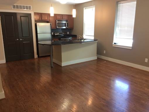 an empty living room with a kitchen with wood floors