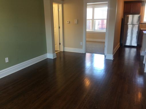 an empty living room with wooden floors and a refrigerator