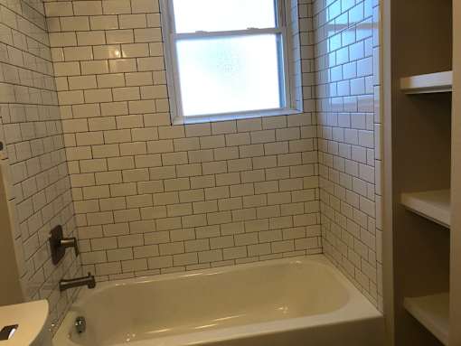 a white tiled bathroom with a tub and a window