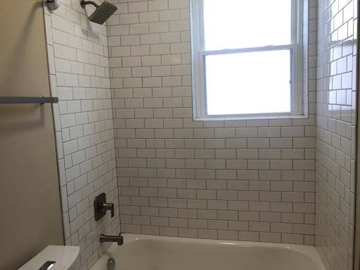 a white tiled bathroom with a window and a bath tub