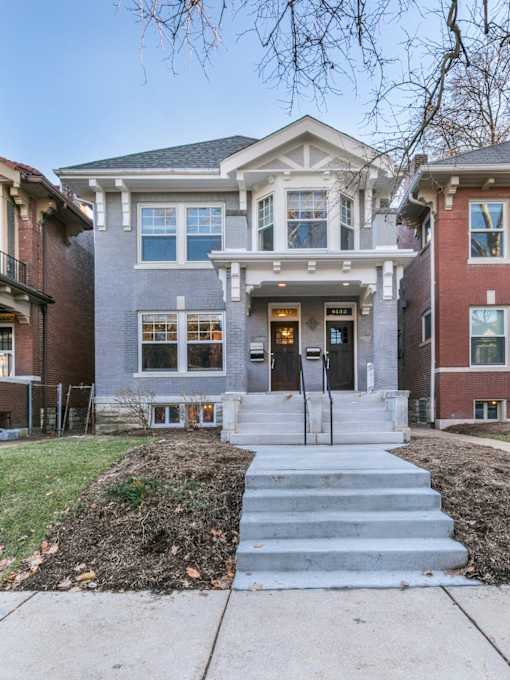 A grey two story house with a black door and steps leading up to it.