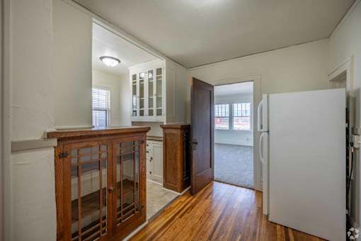 A white refrigerator is in a kitchen with wood floors and cabinets.