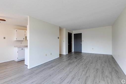 A spacious room with a kitchenette and a door leading to another room.