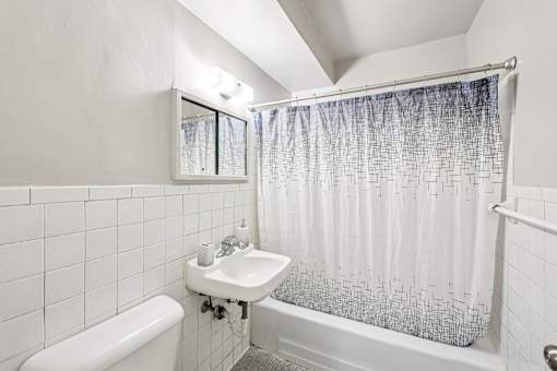 A white bathroom with a white tub, sink, and shower curtain.