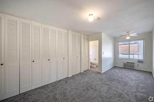 A room with white cupboards and a grey carpet.