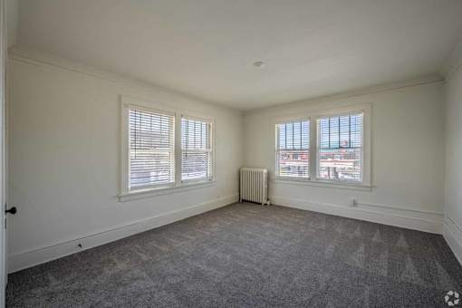 A room with a grey carpet and a window with blinds.