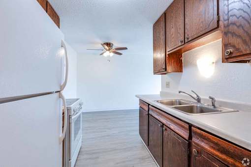 A kitchen with a white fridge, wooden cabinets, and a ceiling fan.