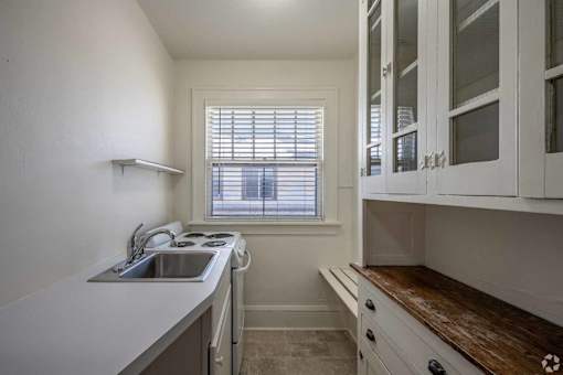 A kitchen with white cabinets and a window with blinds.