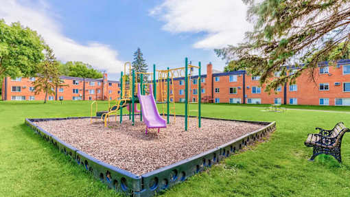A playground with a slide, swings, and a seesaw in front of a building.