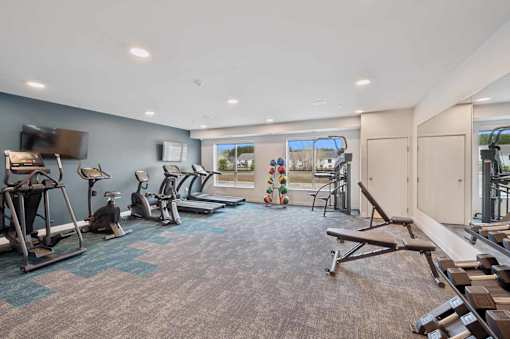 a gym with various machines and weights in a large room with windows