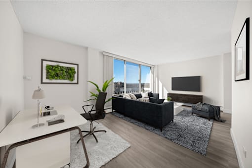 A modern living room with a black couch, a white desk, and a large window.