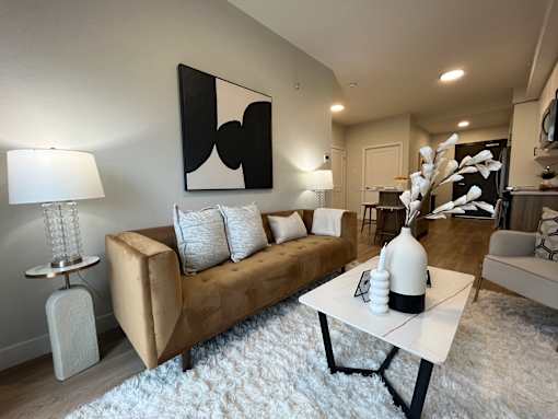 A modern living room with a beige couch, a white coffee table, and a large abstract painting on the wall.