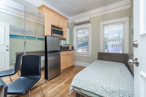 A bedroom with a bed, chair, and a kitchenette.