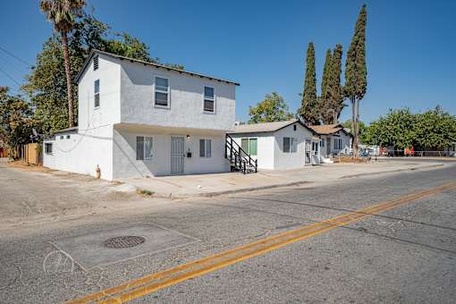 A white house with a grey roof and a tree in front of it.