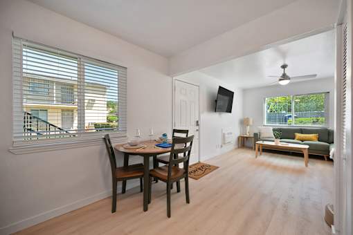A dining room with a table set for two and a couch in the background.