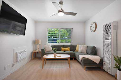 A living room with a grey couch, a wooden table, and a ceiling fan.