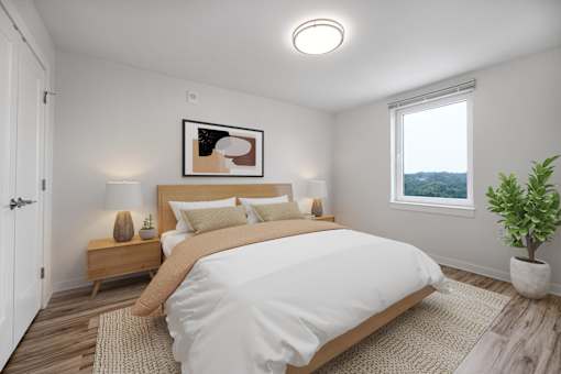A bedroom with a large bed, a nightstand with a lamp, a framed picture on the wall, and a potted plant.