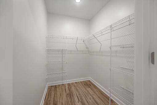 Empty walk-in closet with wooden floor and white shelving.